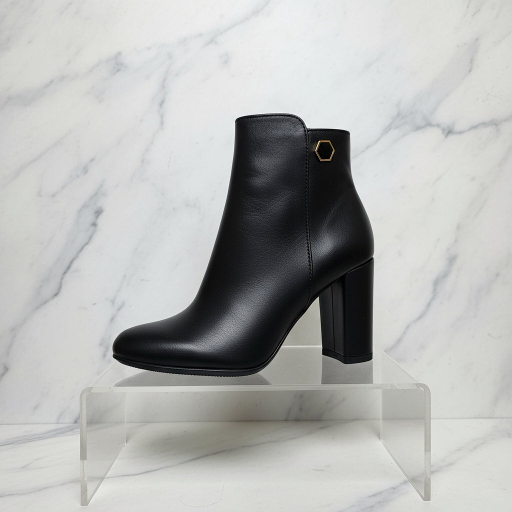 Black petite ankle boot with a gold brooch  on a marble background