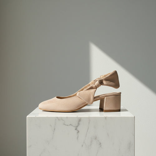 Beige high-heeled shoes with bow detail on a marble pedestal against a gray background