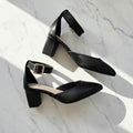 Black high-heeled shoes with a gold buckle on a white background