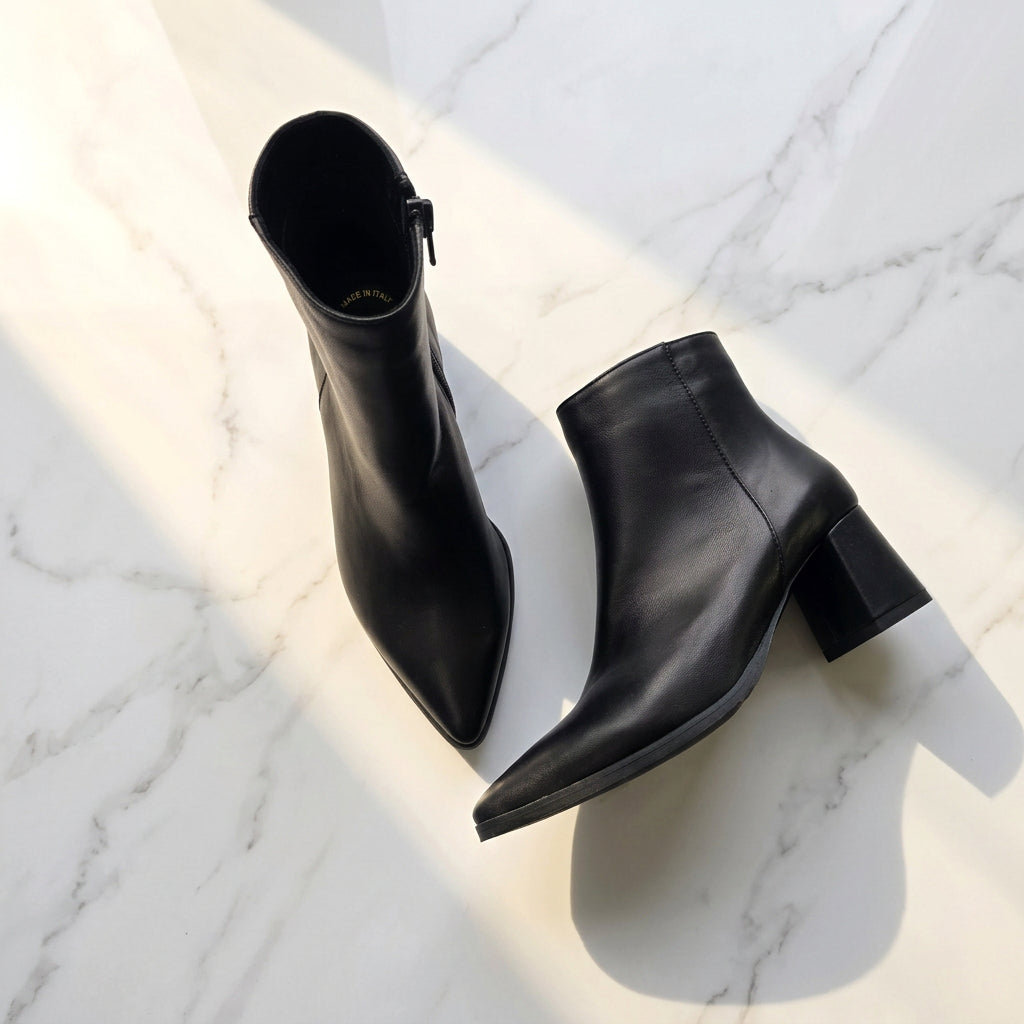 Black pointed toe block heel ankle boots set on a marble floor.