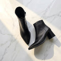 Black pointed toe block heel ankle boots set on a marble floor.