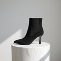 Black ankle boot on a white pedestal against a gray background
