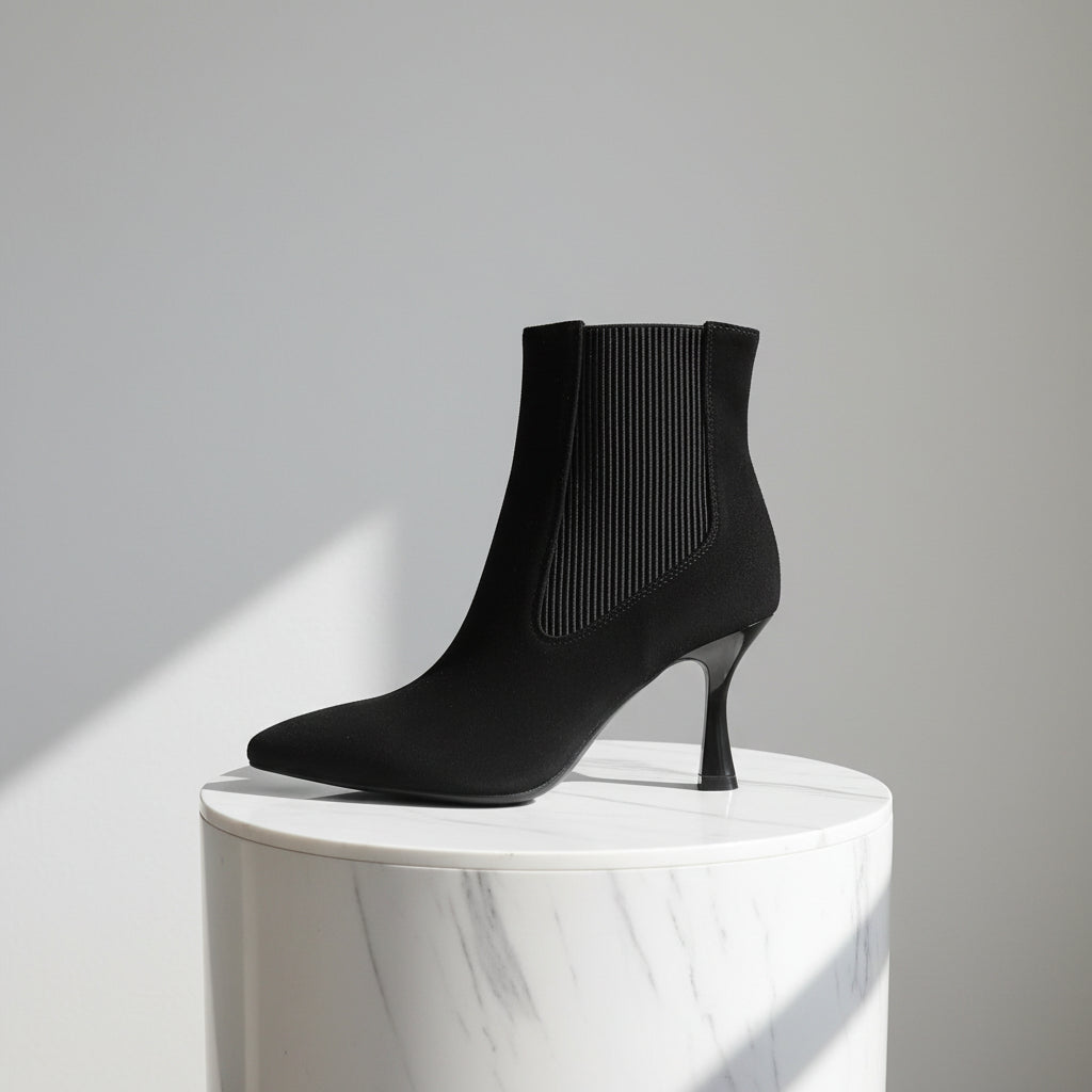 Black high-heeled ankle boot on a white marble pedestal against a gray background