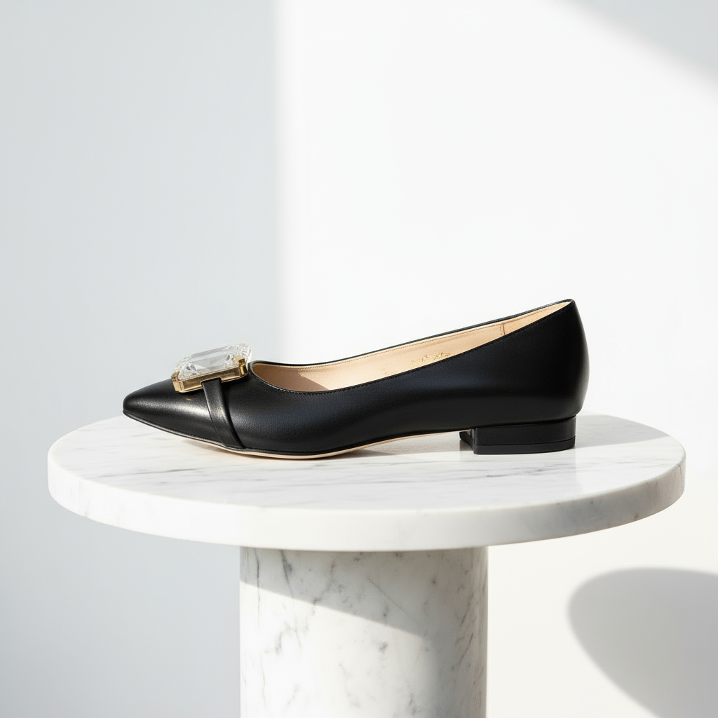 Black flat shoe with a decorative buckle on a white marble pedestal