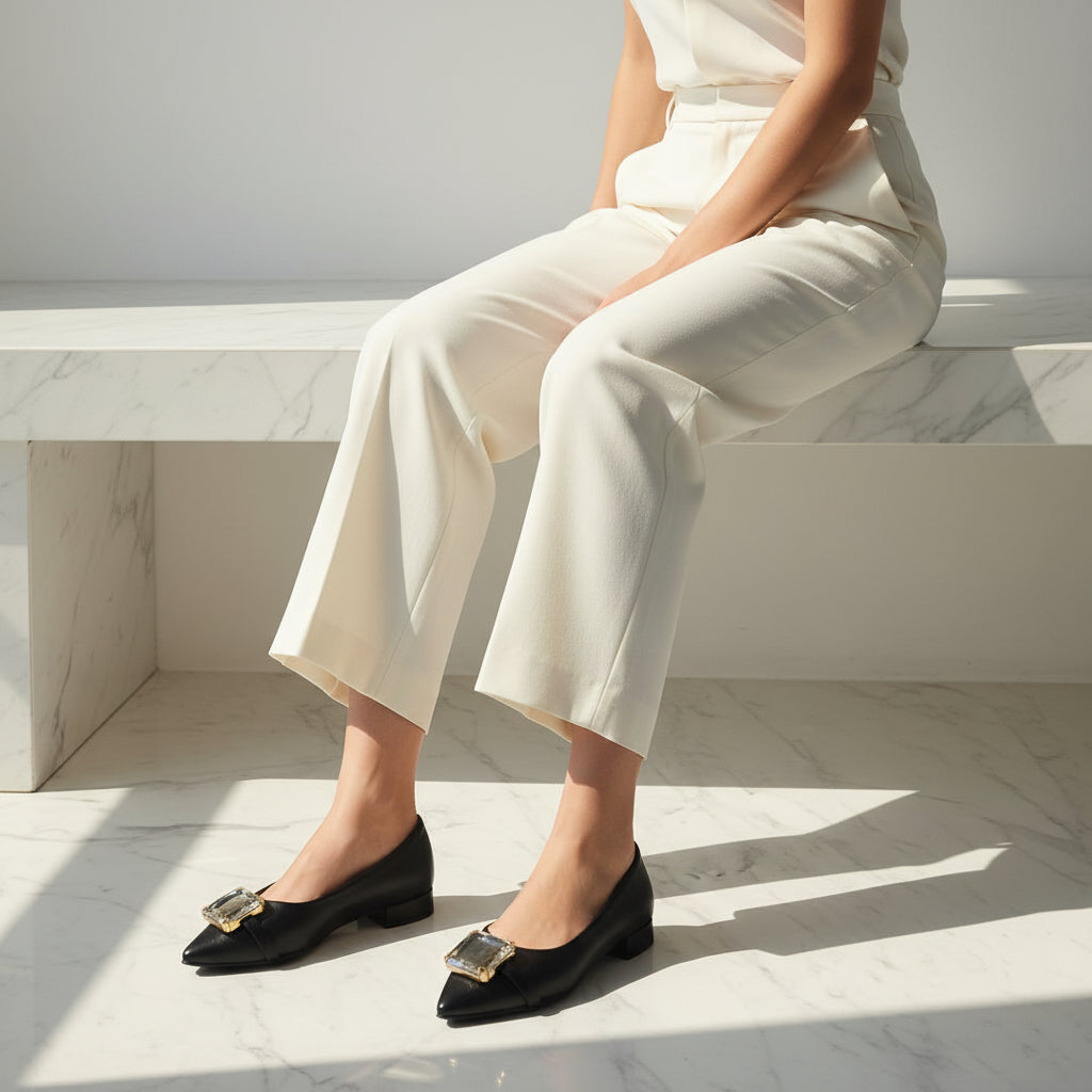 Person wearing black shoes with gold accents sitting on a marble bench.