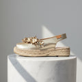 Gold sandal with floral design on a marble pedestal against a gray background