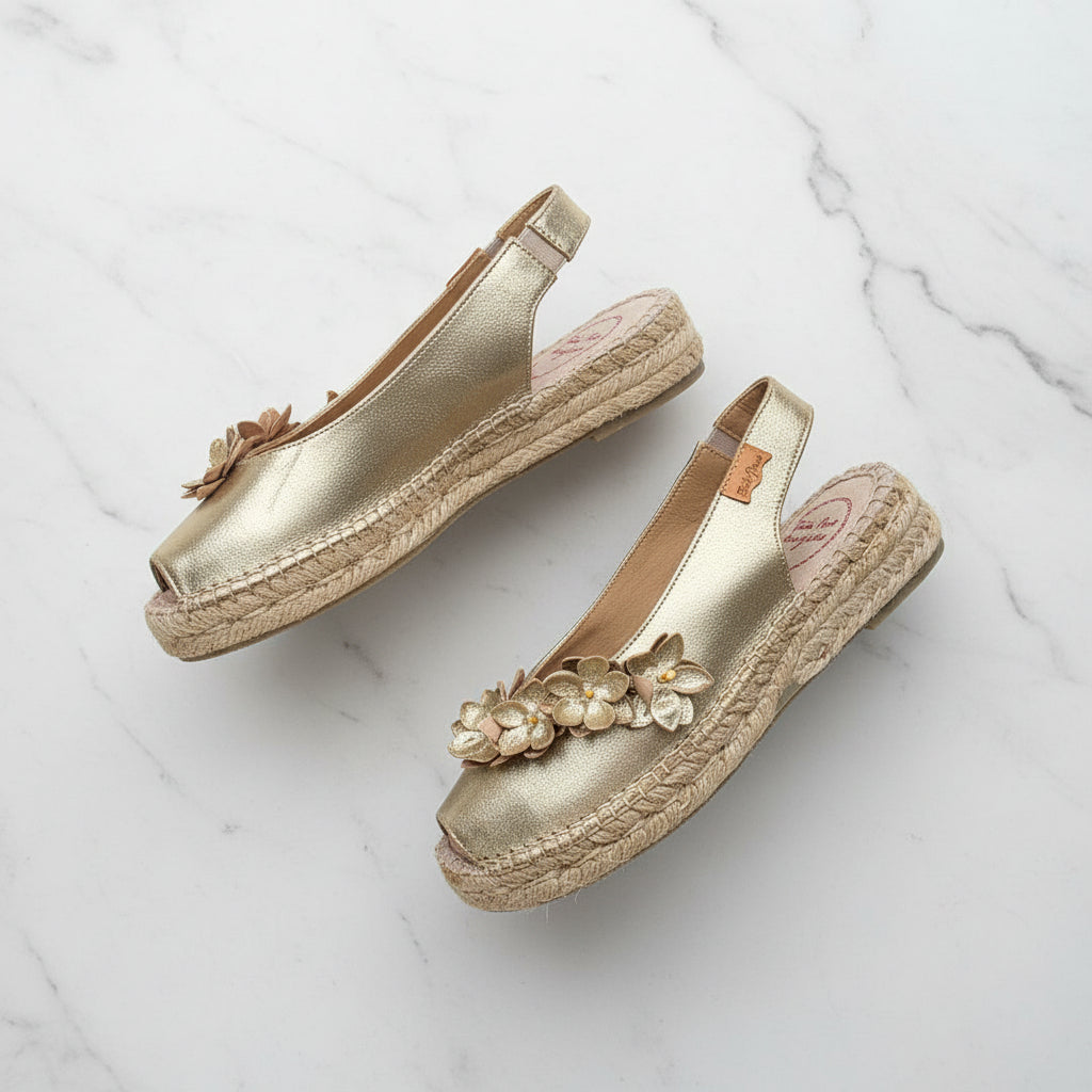 Pair of gold espadrilles with floral embellishments on a dark background