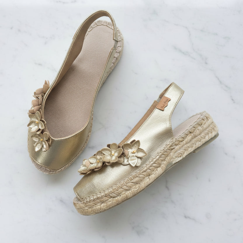 Gold espadrille shoes with floral embellishments on a marble surface