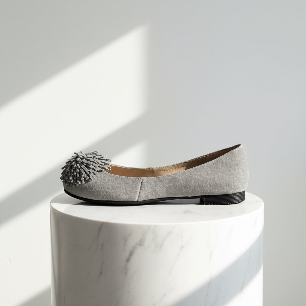 Gray flat shoe with a pom-pom on a white background