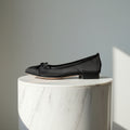 Black leather and mesh ballerina flat shoes set on a marble stand.