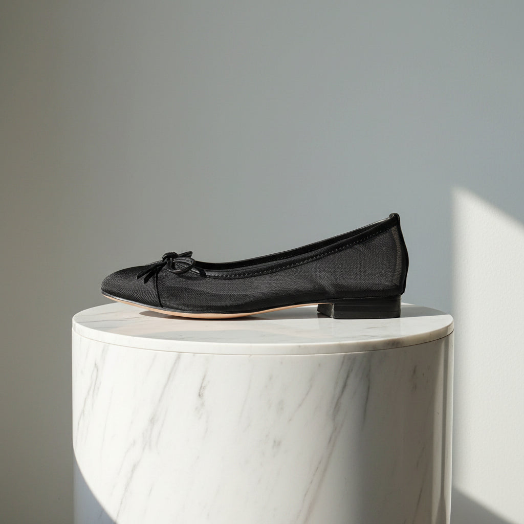 Black leather and mesh ballerina flat shoes set on a marble stand.