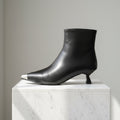 Black leather ankle boot on a white marble block against a neutral background