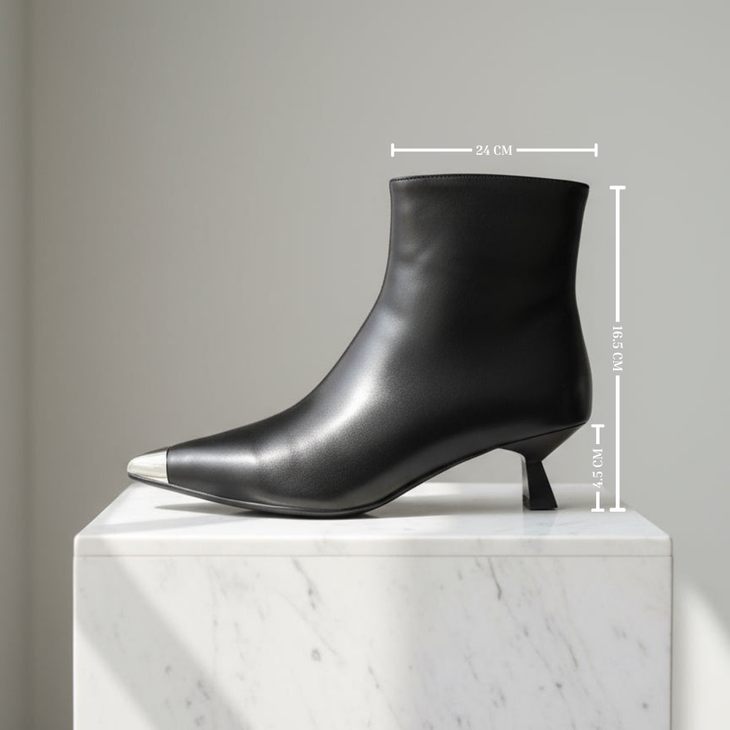 A black leather ankle boot with a pointed toe and silver metal tip, shown on a white marble pedestal with dimension lines indicating measurements of 24 cm width, 105 cm height, and 4 cm heel.