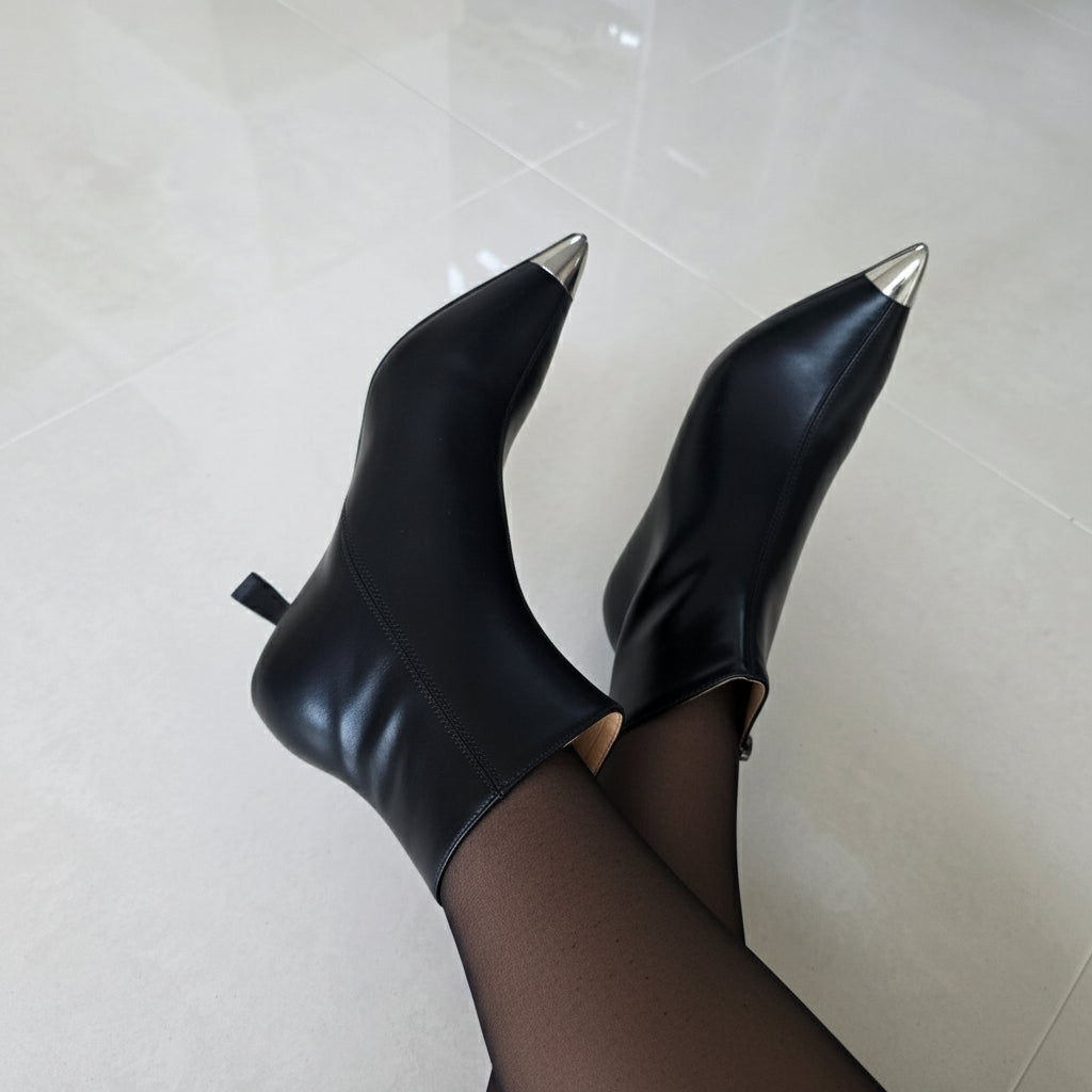 Black pointed-toe boots with metallic tips on a light tiled floor.
