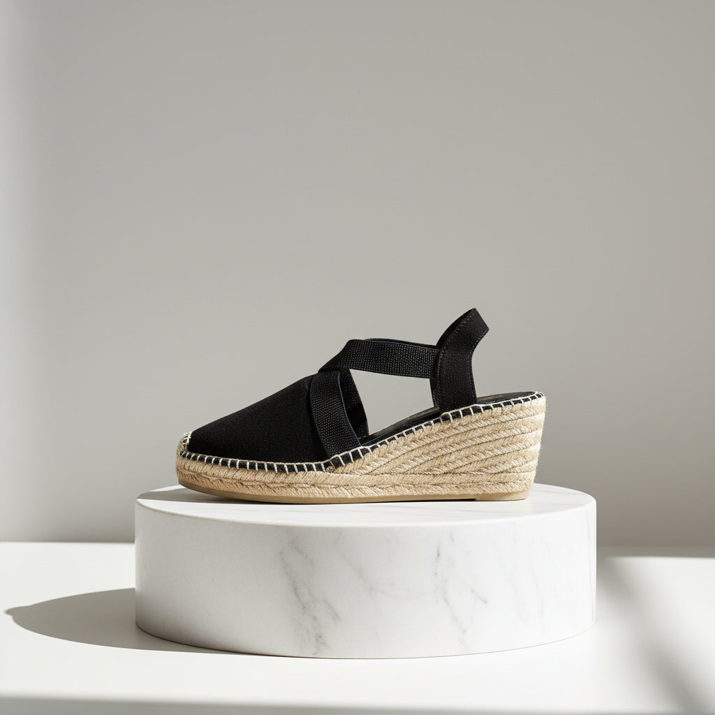 Black wedge sandal with jute sole on a white marble pedestal against a light gray background