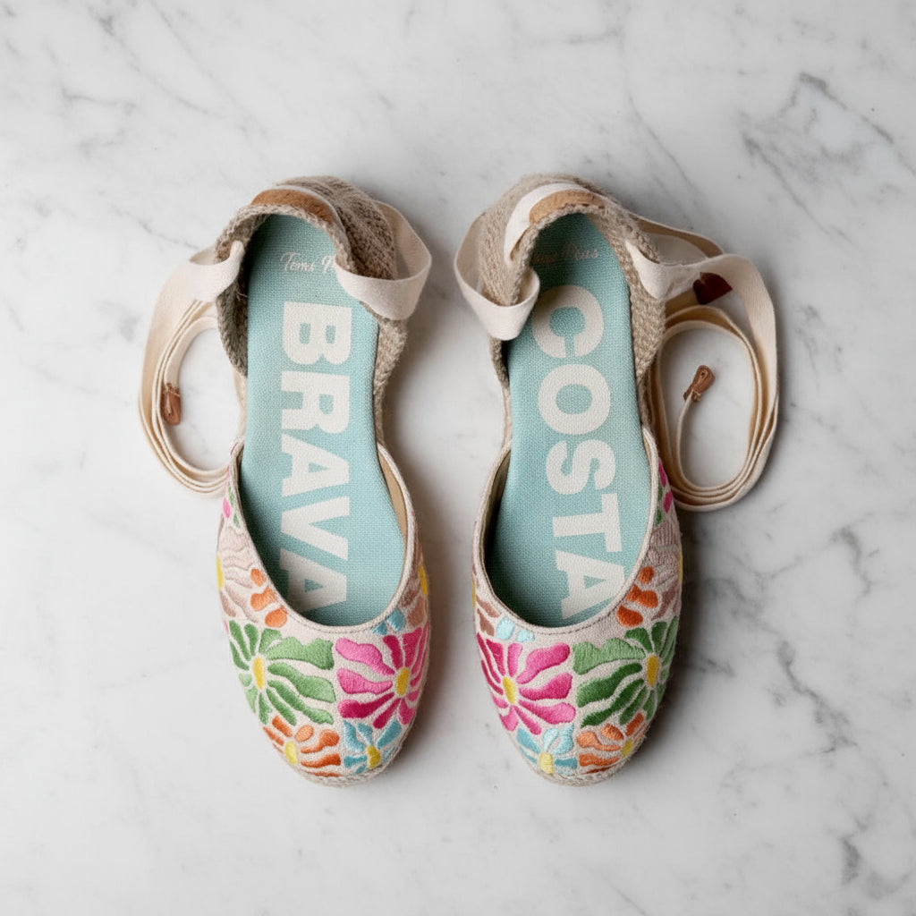 Top view of INDI espadrilles with colorful floral embroidery, cream ankle ties and turquoise insole with COSTA BRAVA branding.