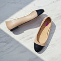 Pair of beige and black flat shoes on a light marble background