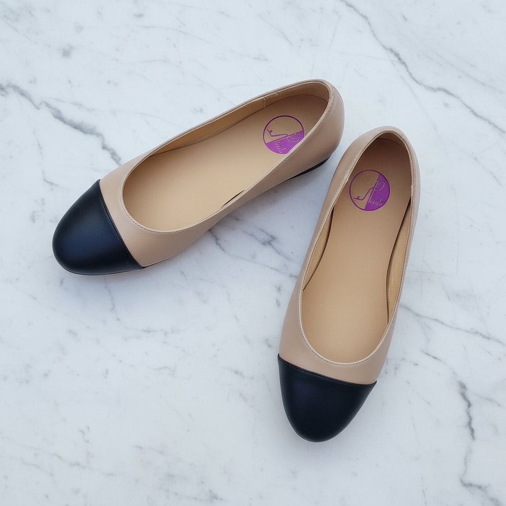 Pair of beige and black flat shoes on a light marble background