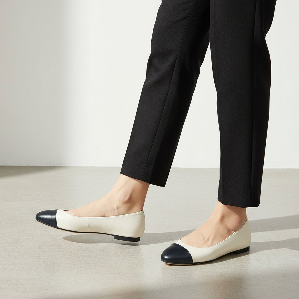 Pair of black and white cap-toe flats on a marble surface