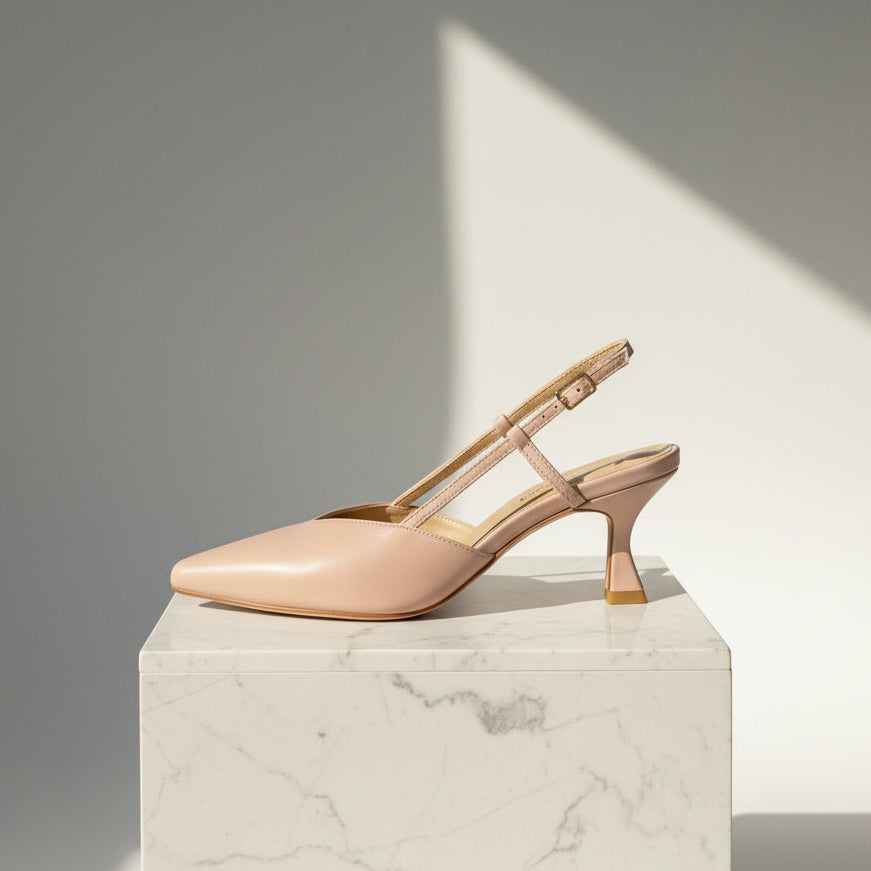 Pair of nude high-heeled slingback shoes on a marble pedestal with a soft shadow background.