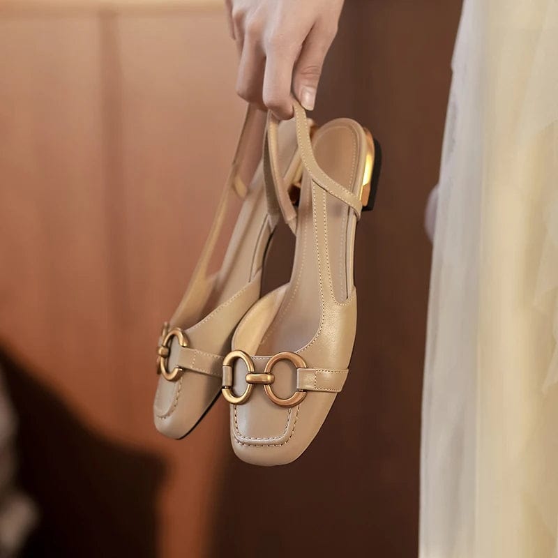 Hand holding beige leather slingbacks with sleek gold metal brooch and elasticated heel strap