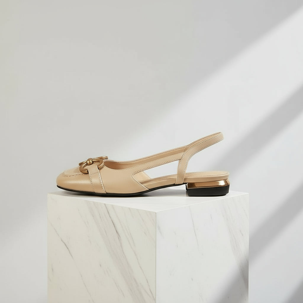 Beige slingback flat shoe on a white marble pedestal with a light gray background