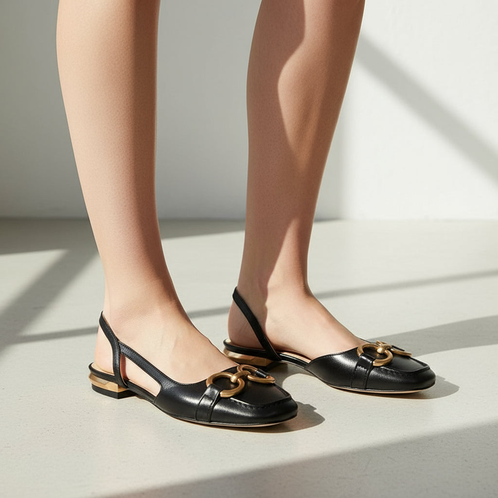 Black slingback flats with gold chain detail on a marble surface