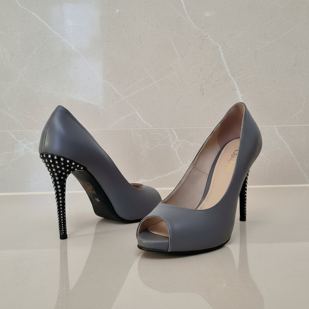 Pair of gray high-heeled shoes with studded details on a light marble background