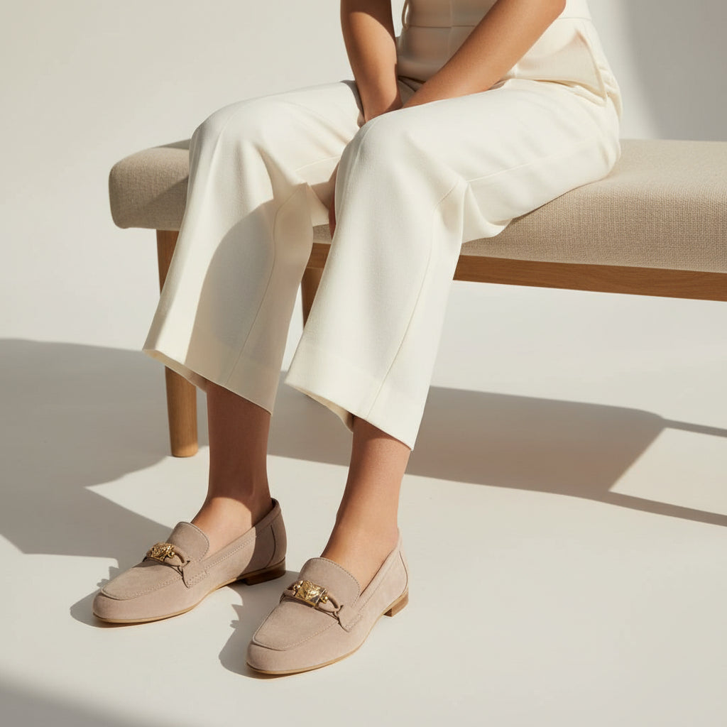 Person wearing beige loafers with gold accents sitting on a bench.