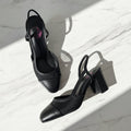 KAI black leather and mesh slingback block heel shoes flat lay on marble surface.