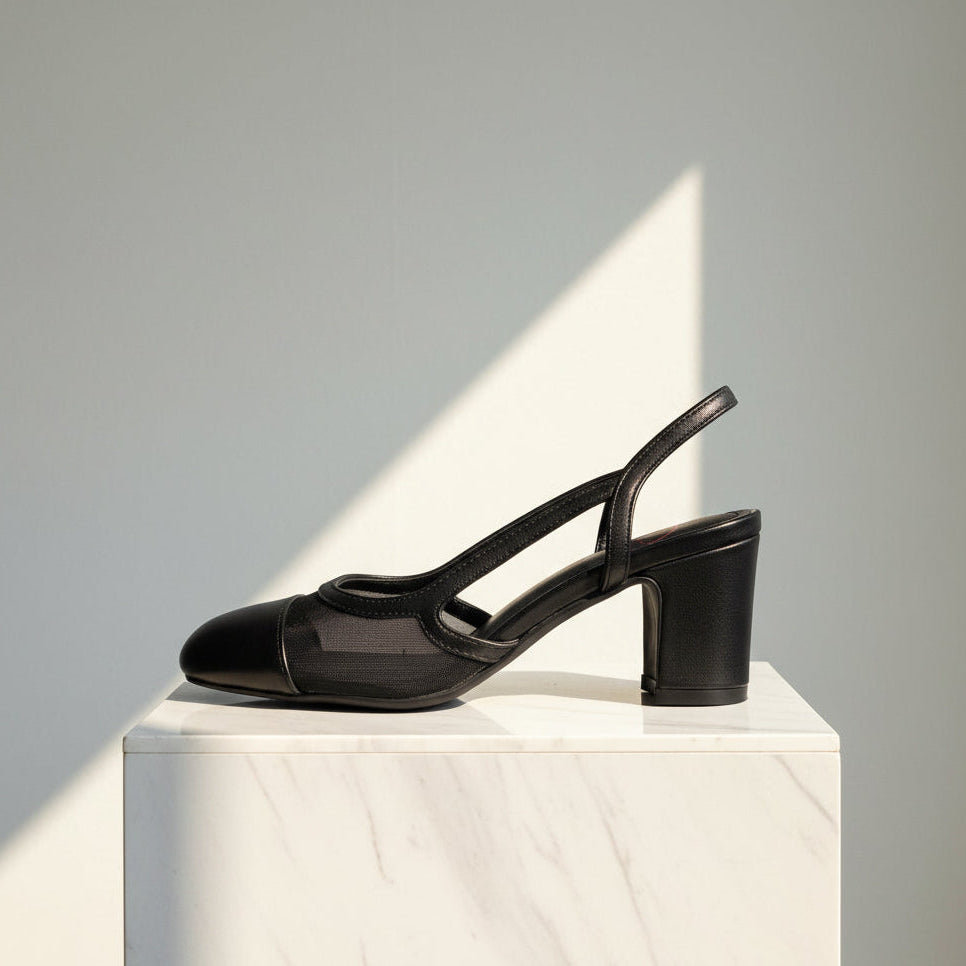 Black leather and mesh high-heeled shoe on a white pedestal against a grey background
