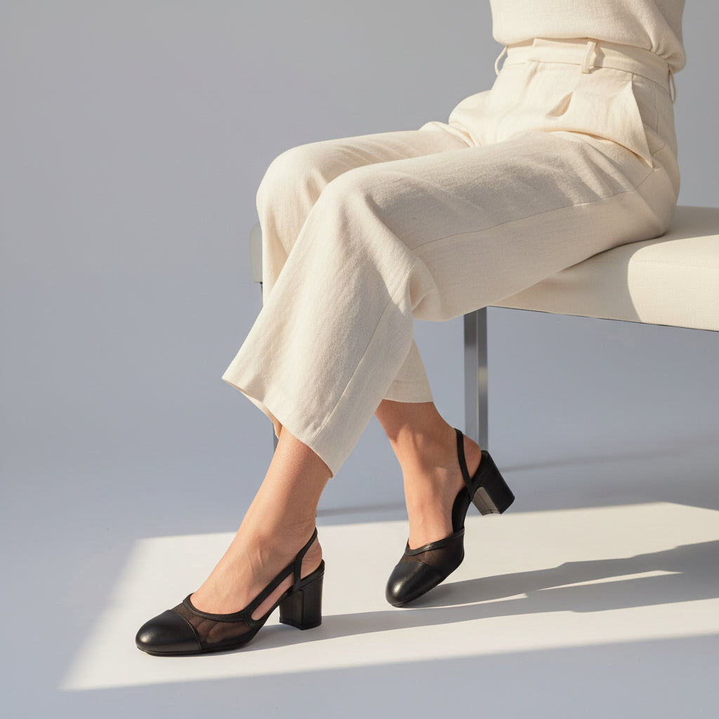 KAI black leather and mesh slingback block heel shoes worn by seated model in beige trousers.
