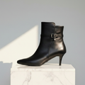 Petite black leather kitten heel ankle boots set on a light grey marble pedestal. 