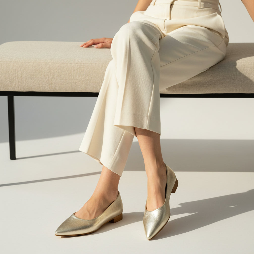 Person wearing gold flats and white pants sitting on a bench.
