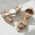 Beige high-heeled sandals with bow details on a marble surface