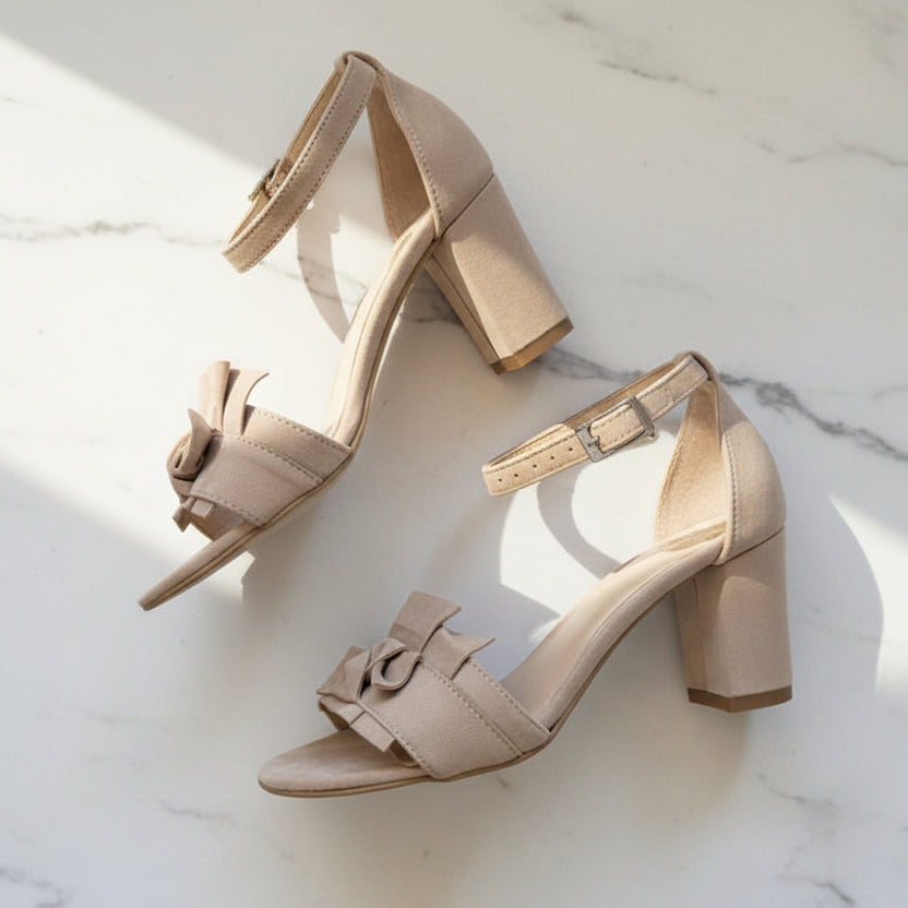 Pair of beige high-heeled sandals with bow details on a marble surface