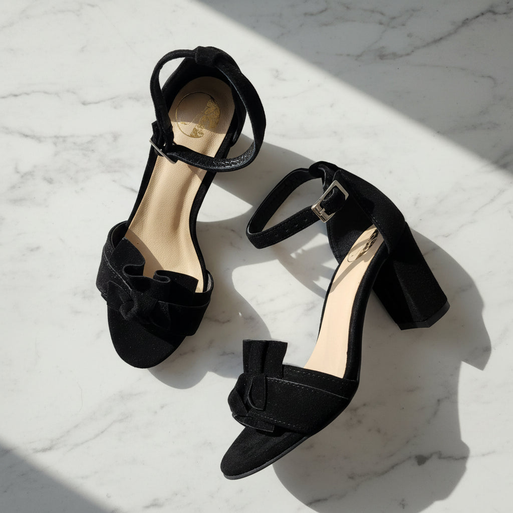 Black high-heeled shoes with bow details on a marble surface