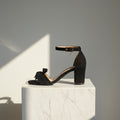 Black sandal with a block heel on a white marble pedestal against a gray background