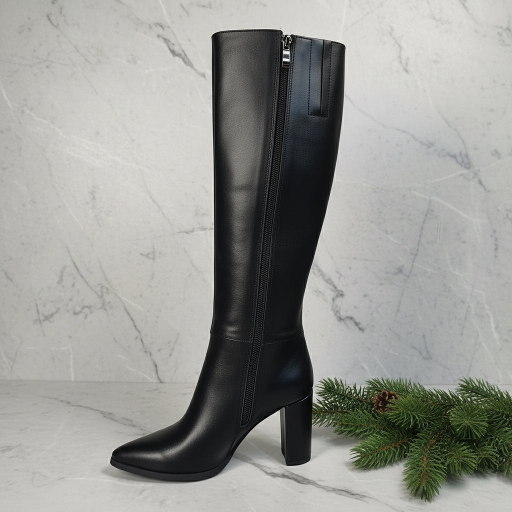 Black knee-high boot on a white surface with a blurred indoor background