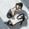 Black high-heeled sandals on a light gray background