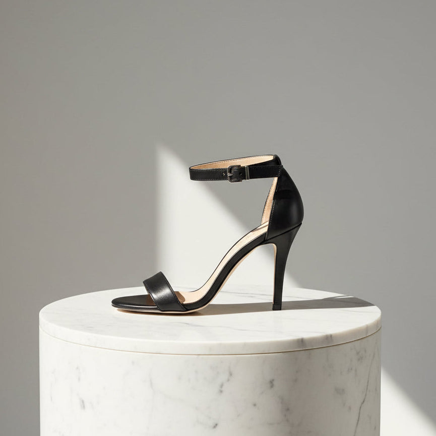 Black high-heeled sandal on a white marble pedestal against a gray background