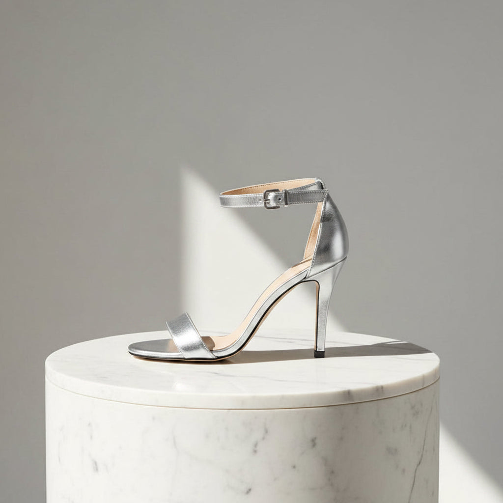 Silver high-heeled sandal on a marble pedestal with a neutral background