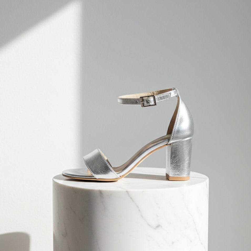 Silver high-heeled sandal on a white marble pedestal against a light gray background