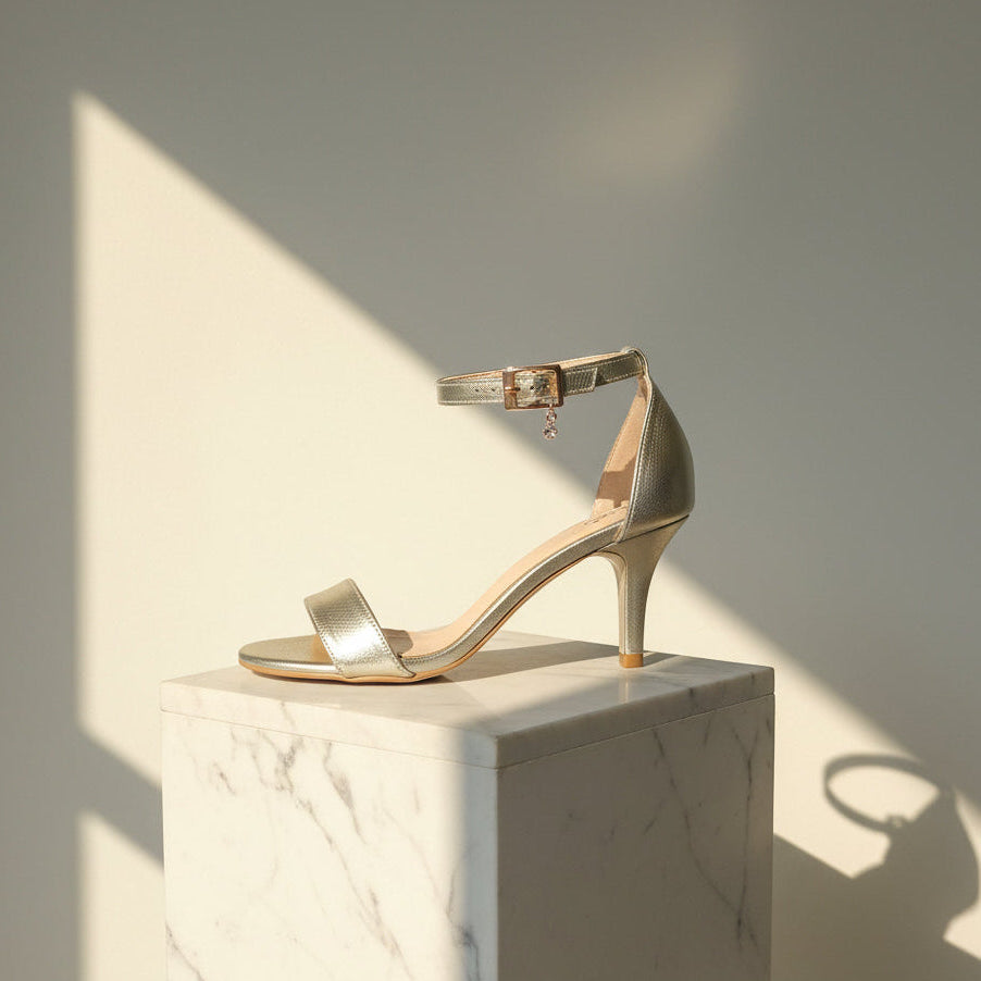 Gold high-heeled sandal on a marble surface with a soft light background
