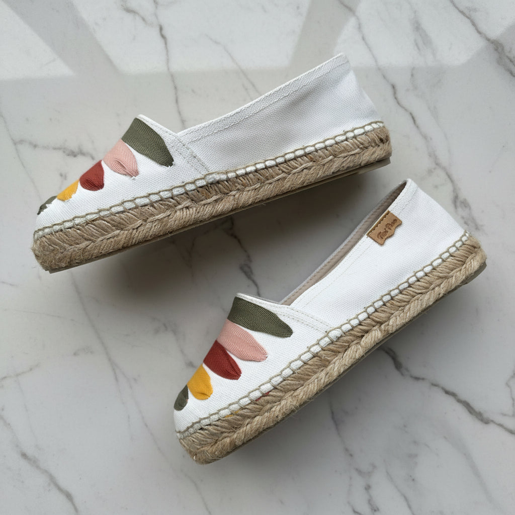 Pair of white espadrilles with colorful accents on a marble surface