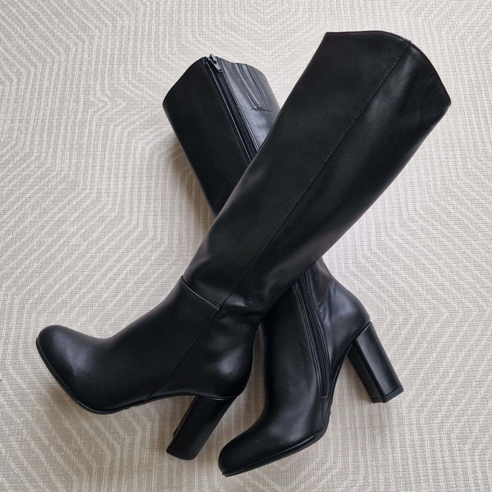 Knee-high black leather boots set on a high block heel. 