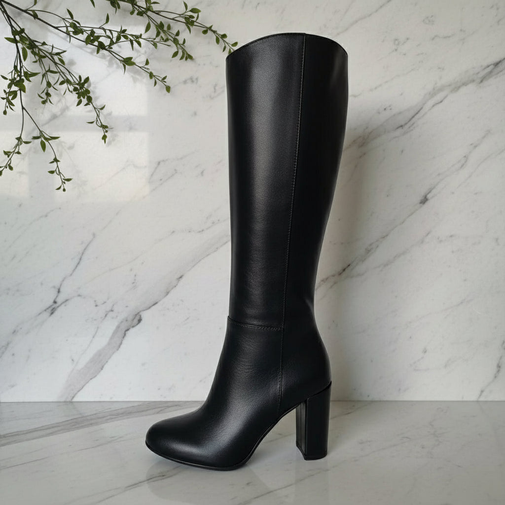 Black knee-high boot on a white platform with a blurred indoor background