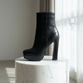 Black high-heeled ankle boot on a marble surface with a neutral background