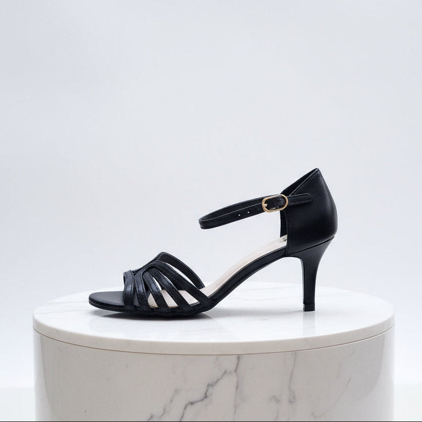 Black sandal with a thin strap on a white marble pedestal