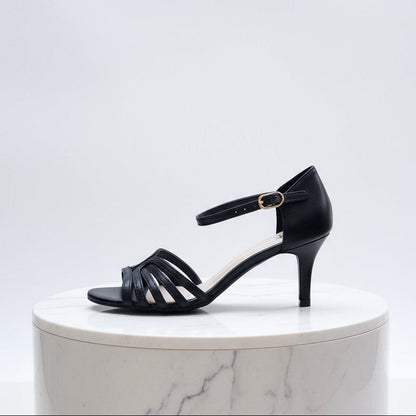 Black sandal with a thin strap on a white marble pedestal